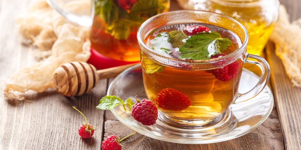 A cup of herbal tea with honey and fresh raspberries