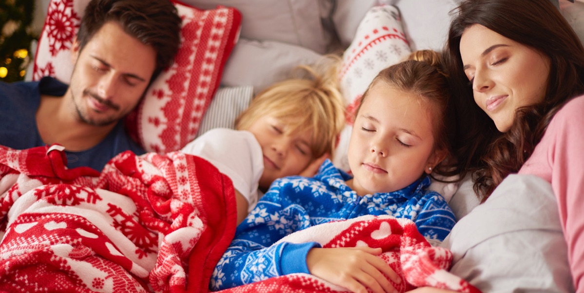 A family wearing winter pajamas sleeping in front of a fire