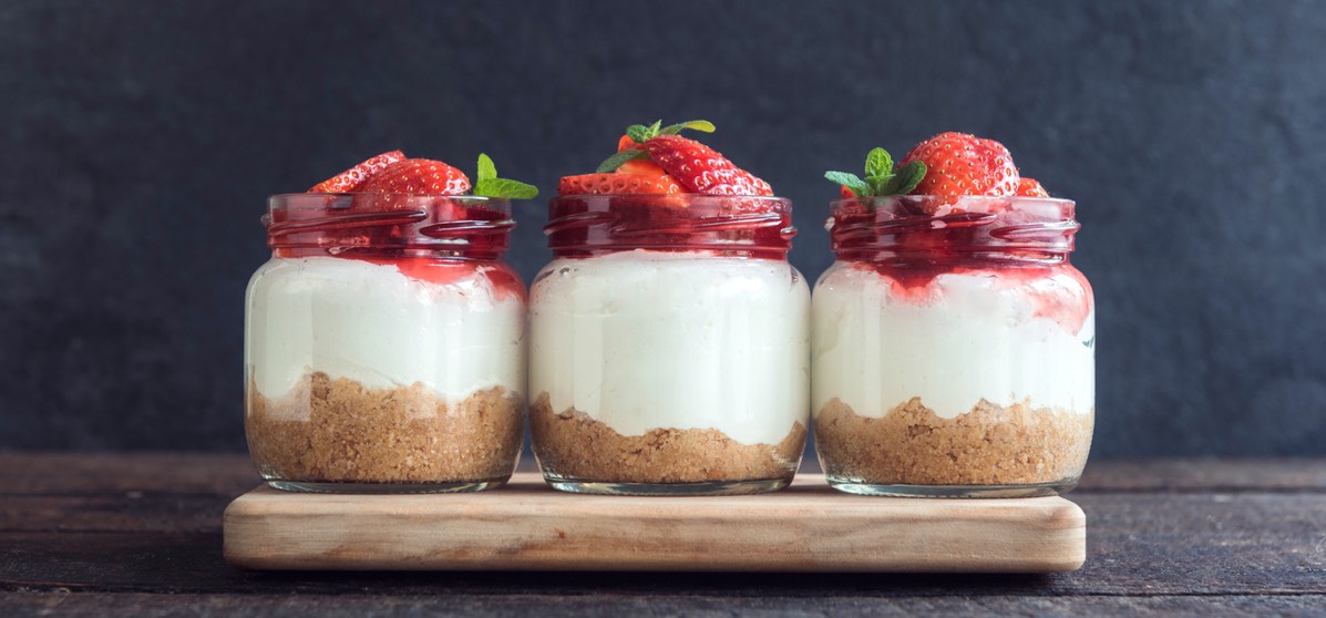 Three cheesecakes made in small mason jars and topped with fresh strawberries